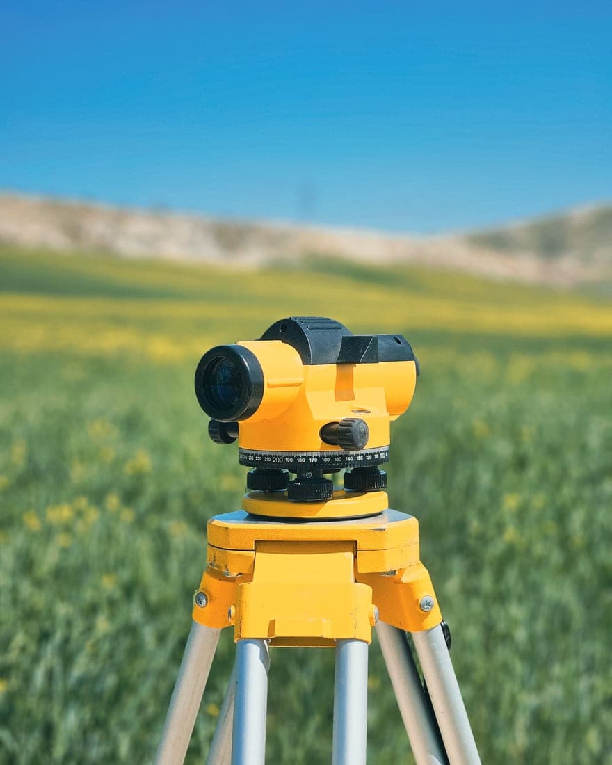 Equipamento óptico de levantamento topográfico montado em tripé, em campo aberto